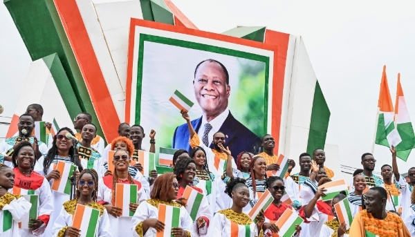 Supporters stand next to a photo of Ivorian President Alassane Ouattara during a military parade marking the 65th anniversary of Ivory Coast's independence in Bouaké on 7 August 2025.