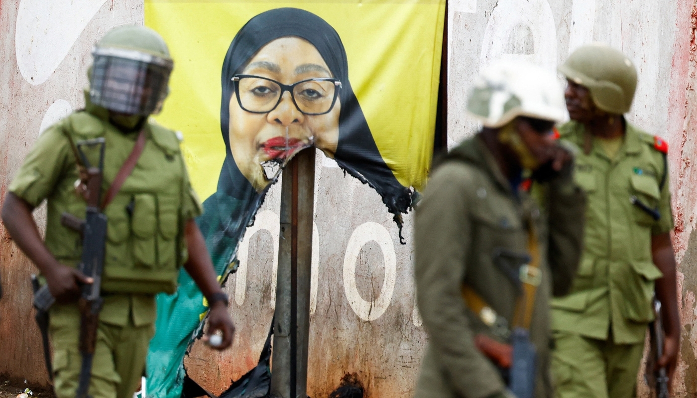 Tanzanian riot police next to a vandalised campaign poster of President Hassan in Namanga, Tanzania, on 30 October 2025.