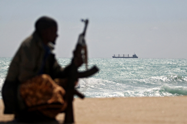 An armed Somali pirate along the coast, 7 January 2010. In the background, the Greek cargo ship MV Filitsa is anchored off the town of Hobyo in northeast Somalia, where it is being held by pirates.