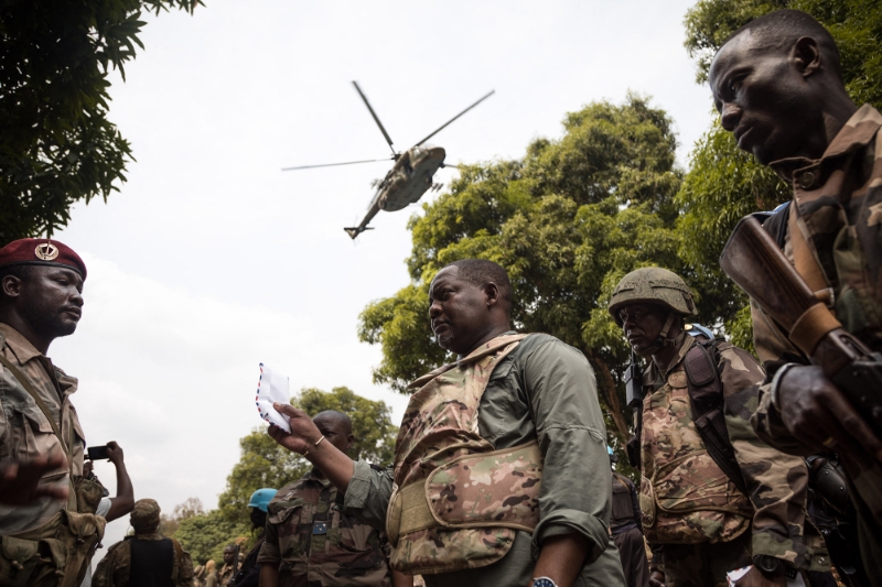 The then Prime Minister of the Central African Republic, Firmin Ngrebada (centre), salutes his troops as a Russian-made support helicopter flies overhead on the road between Boali and Bangui on 10 January 2021.