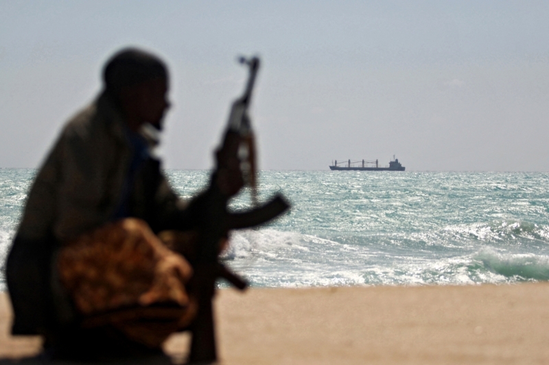An armed Somali pirate along the coast, 7 January 2010. In the background, the Greek cargo ship MV Filitsa is anchored off the town of Hobyo in northeast Somalia, where it is being held by pirates.